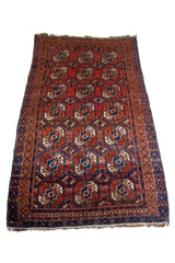 Alfombra Persa Bukara rojo y marrón de 0.85 x 1.45 mts, detalle de guarda, borde y textura; el diseño muestra hileras de medallones ovalados sobre un campo rojo y marrón con guardas geométricas oscuras