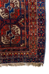Alfombra Persa Bukara rojo y marrón de 0.85 x 1.45 mts, detalle cercano de motivos y terminación; el diseño muestra hileras de medallones ovalados sobre un campo rojo y marrón con guardas geométricas oscuras