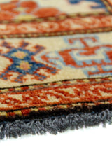 Alfombra Caucasica Kazak beige y azul de 0.83 x 1.30 mts, detalle cercano de motivos y terminación; el diseño muestra medallones geométricos azules sobre un campo beige con guardas de acento ladrillo