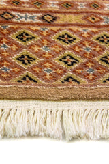 Alfombra Persa Bukara marrón de 0.99 x 1.60 mts, detalle cercano de los motivos del campo y la combinación de tonos