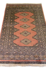 Alfombra Persa Bukara rosado y gris de 0.94 x 1.60 mts, vista en perspectiva que permite apreciar el campo central y las guardas