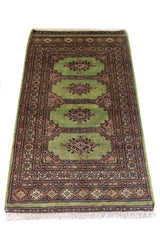 Alfombra Persa Bukara verde y rosa de 0.76 x 1.30 mts, vista en perspectiva que permite apreciar el campo central y las guardas