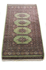 Alfombra Persa Bukara verde y rosa de 0.76 x 1.30 mts, detalle cercano de los motivos del campo y la combinación de tonos