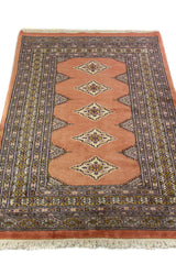 Alfombra Persa Bukara marrón y gris de 0.92 x 1.42 mts, vista en perspectiva que permite apreciar el campo central y las guardas