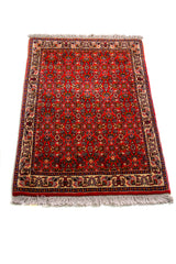 Alfombra Persa Horazan rojo y beige de 0.48 x 0.69 mts, vista en perspectiva que permite apreciar el campo central y las guardas