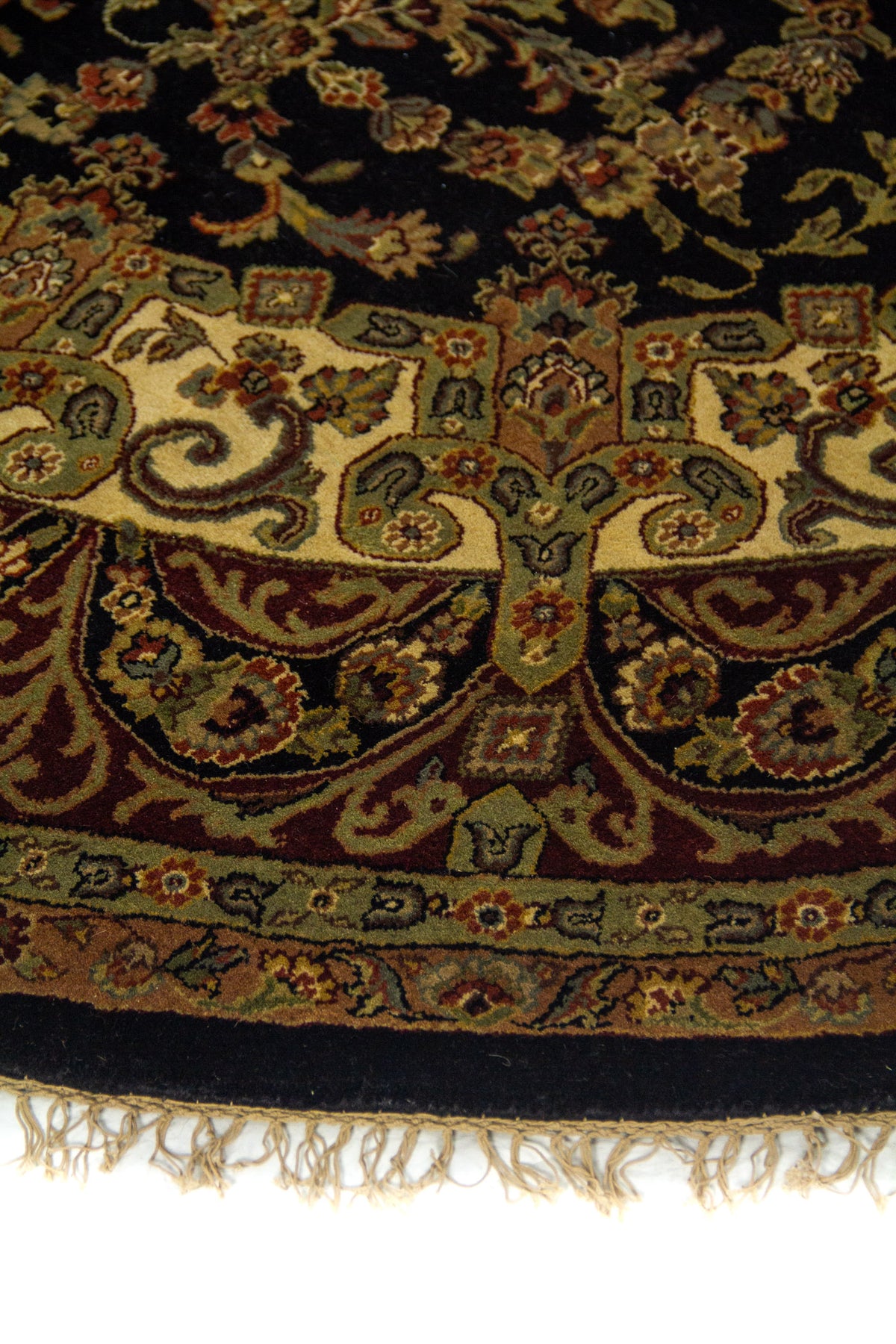 Detalle de borde de alfombra redonda con diseño floral en tonos beige, verde oliva y rojo vino.