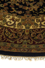 Detalle de borde de alfombra redonda con diseño floral en tonos beige, verde oliva y rojo vino.