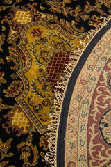 Detalle de alfombra redonda plegada con medallón dorado, fondo negro y guarda ornamental.