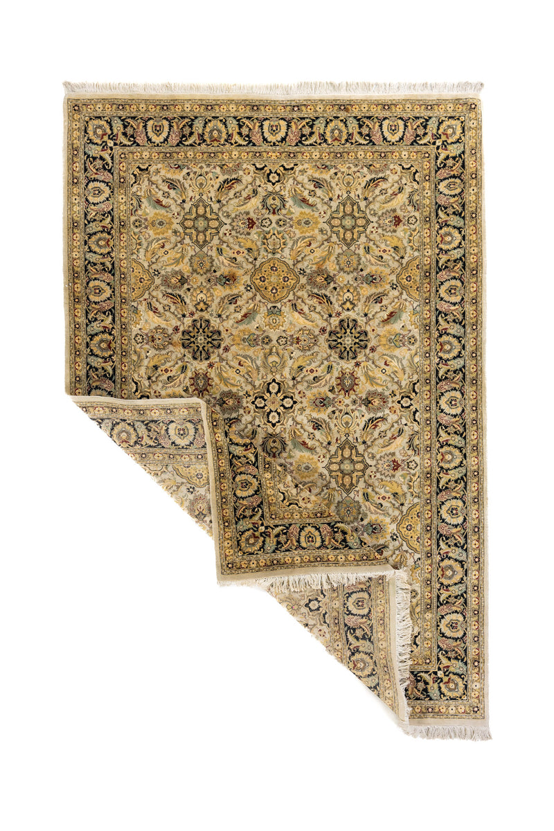 Alfombra beige de inspiración oriental con una esquina levantada, mostrando el reverso, los flecos y el espesor del tejido.