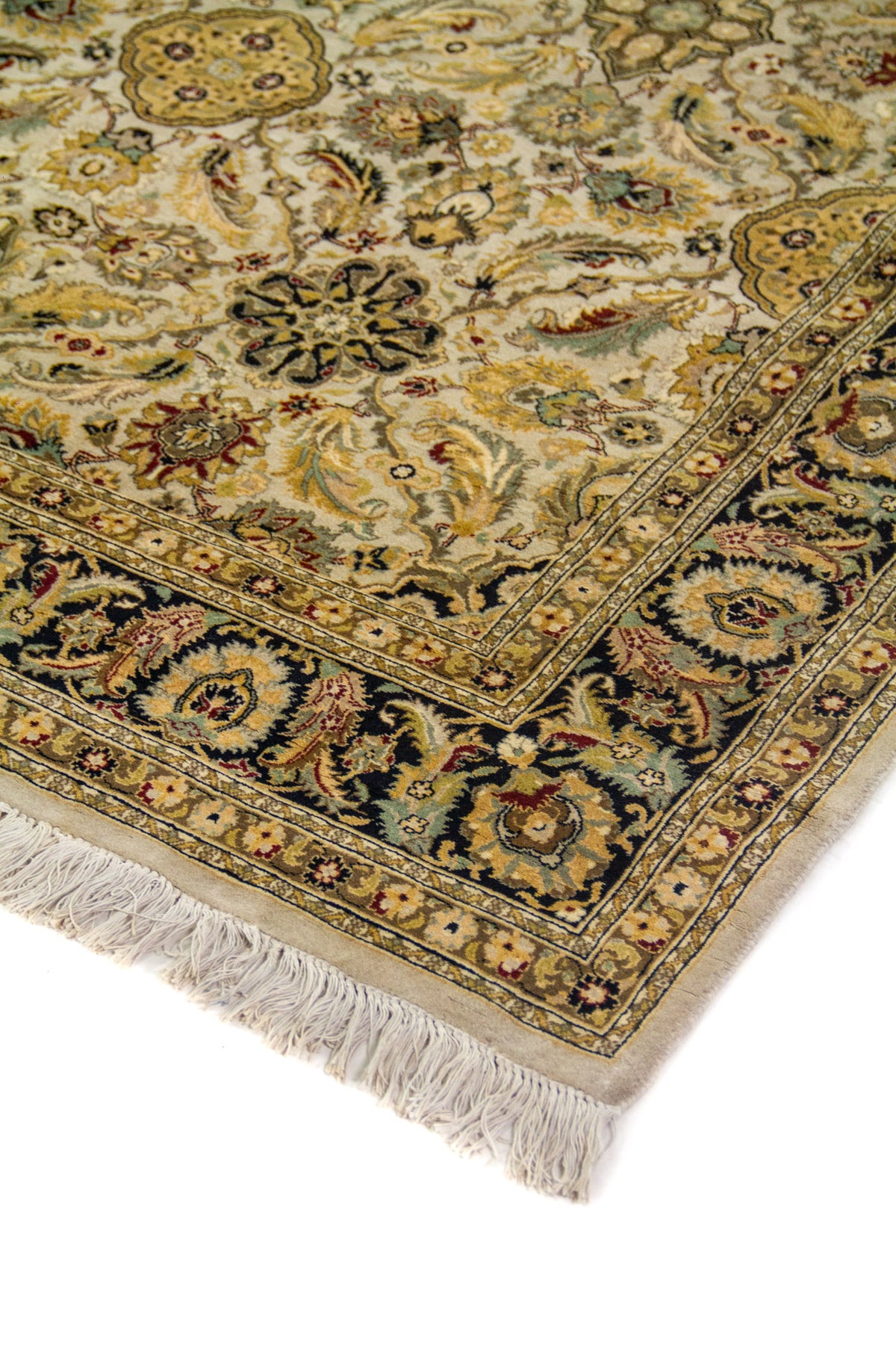 Detalle en perspectiva de alfombra beige con motivos florales delicados, borde oscuro ornamental y flecos claros.