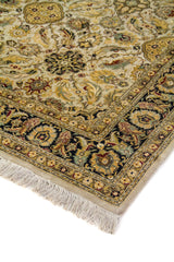 Detalle en perspectiva de alfombra beige con motivos florales delicados, borde oscuro ornamental y flecos claros.