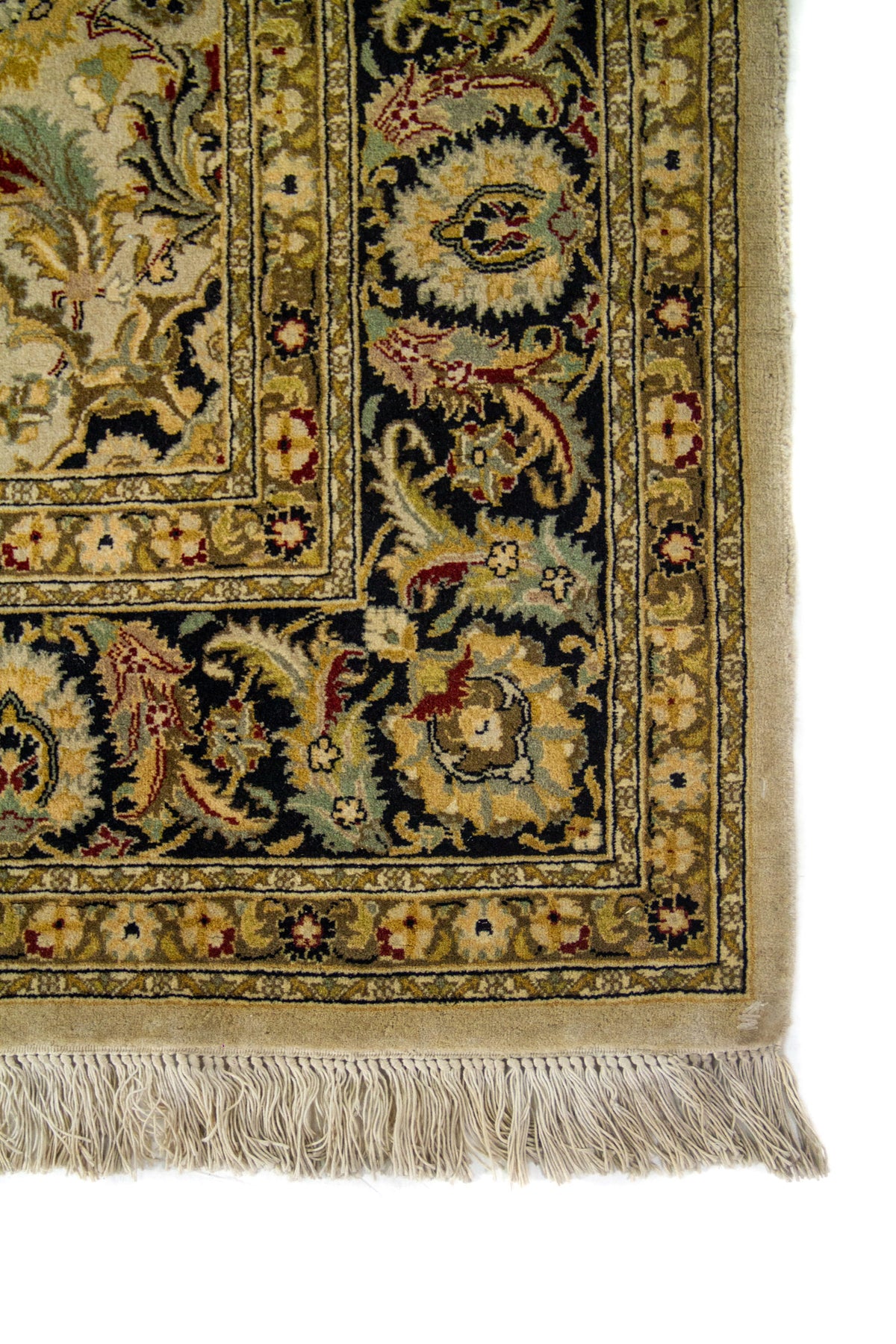 Primer plano de esquina de alfombra oriental con marco oscuro, ornamentos florales y terminación con flecos beige.