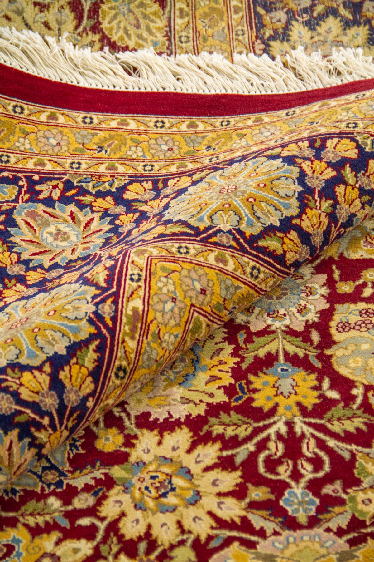 Esquina doblada mostrando textura y grosor, guarda azul marino con flores y flecos beige