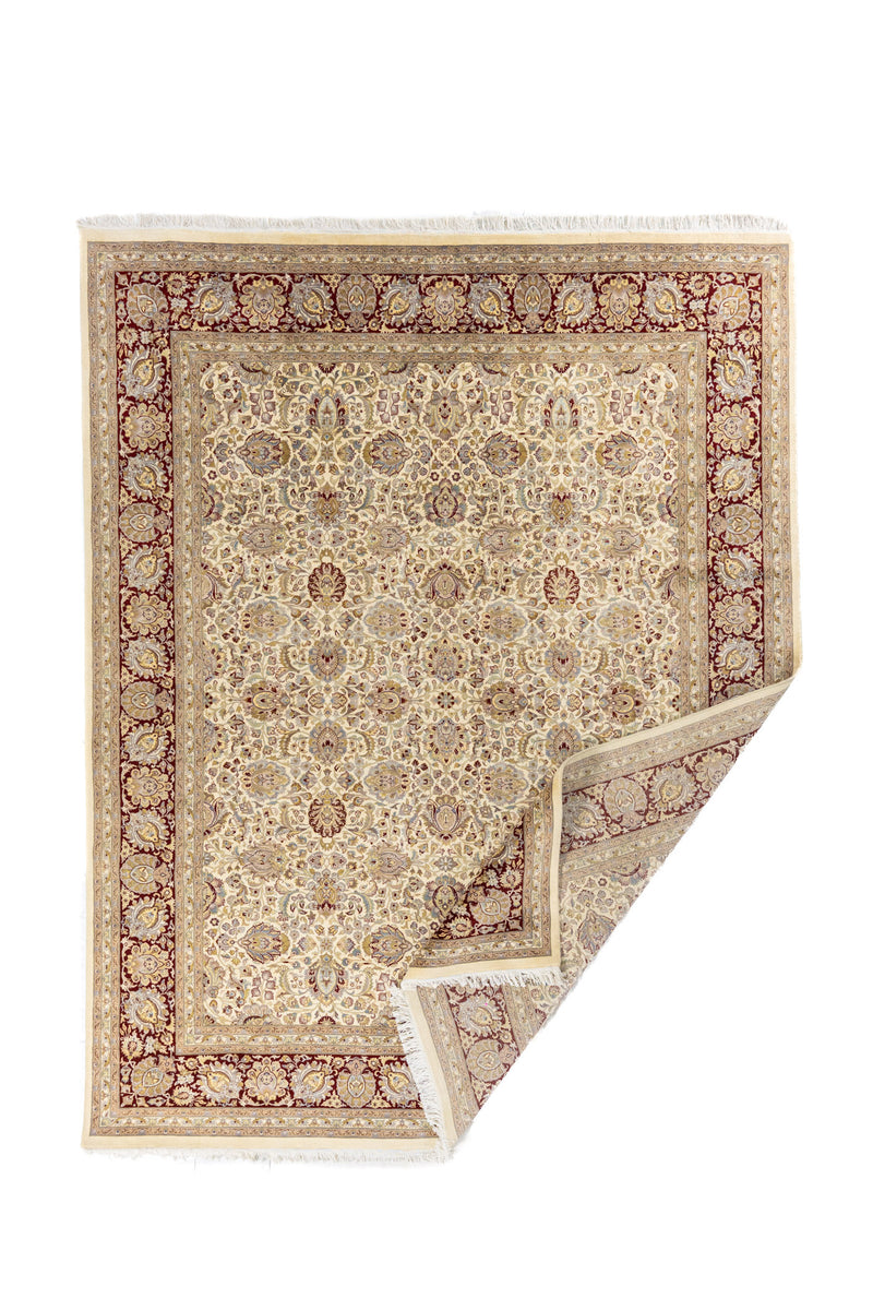 Alfombra con esquina doblada mostrando el reverso, el borde y la terminación con flecos claros.