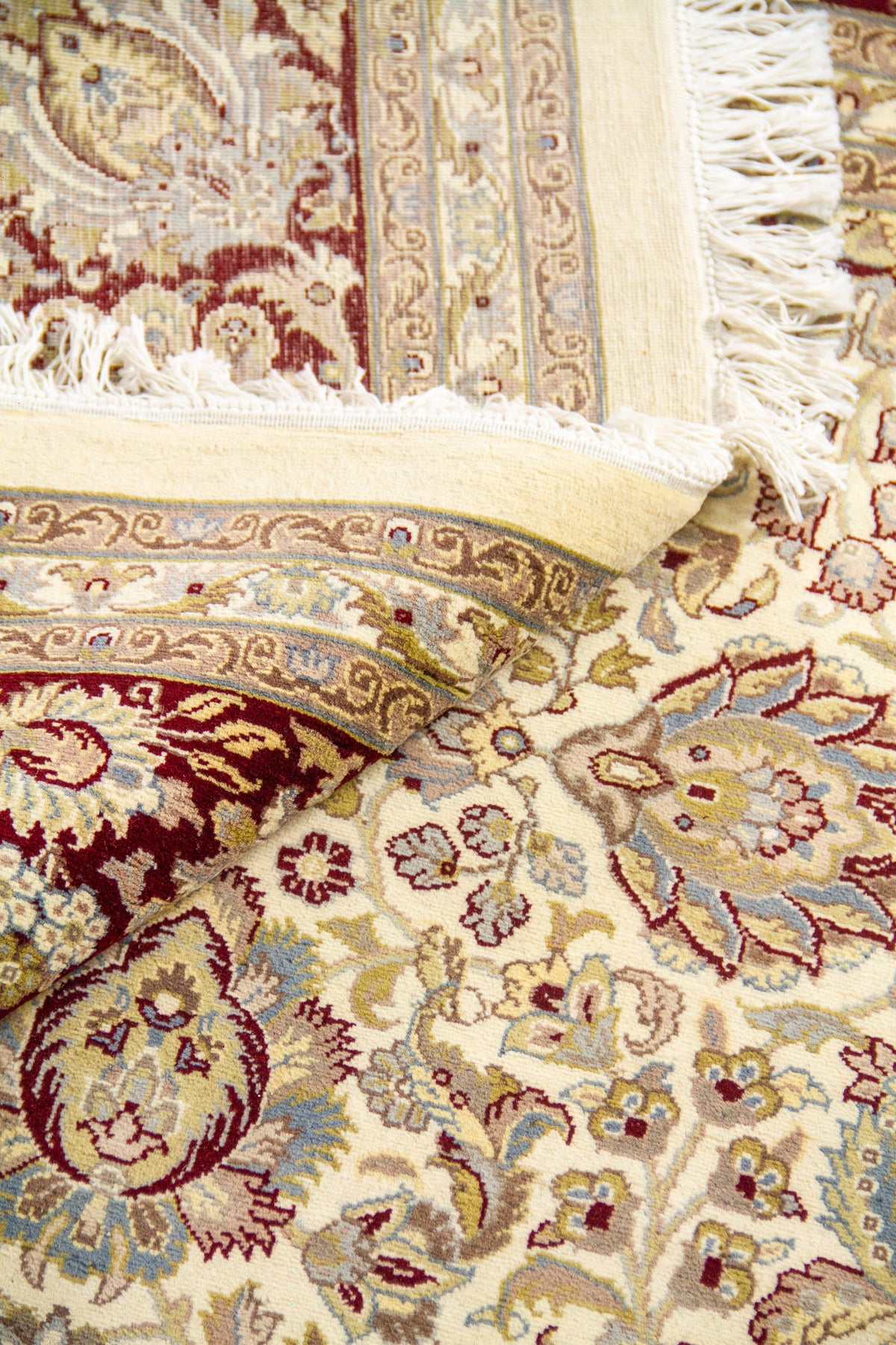 Detalle del tejido y flecos, mostrando la densidad del nudo y los colores beige, blanco, rojo y azul suave.