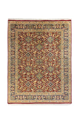 Alfombra clásica de estilo persa con fondo rojo, motivos florales en azul y beige, y guarda decorativa azul marino sobre fondo claro.
