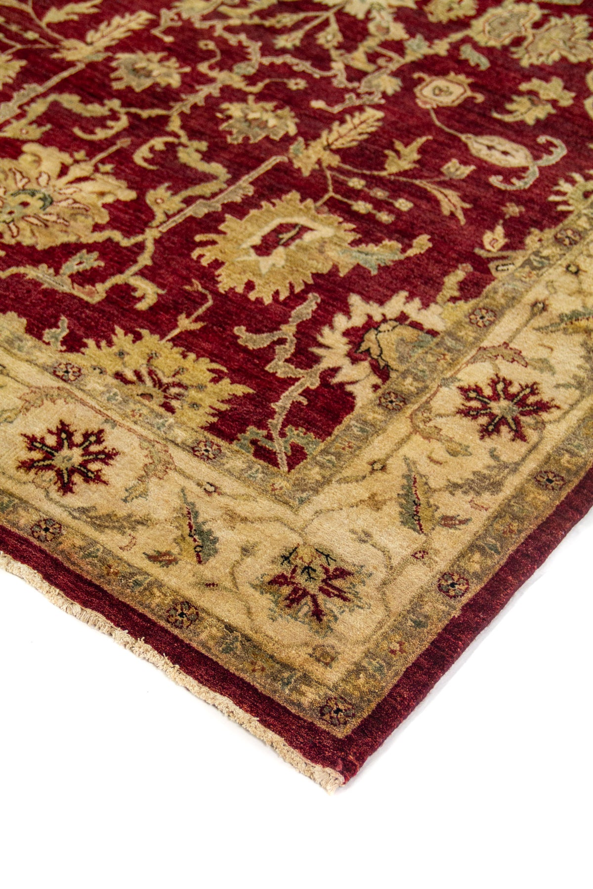 Detalle en perspectiva de alfombra roja con diseño vegetal tradicional, borde beige y flecos claros.