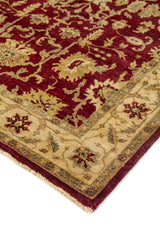 Detalle en perspectiva de alfombra roja con diseño vegetal tradicional, borde beige y flecos claros.