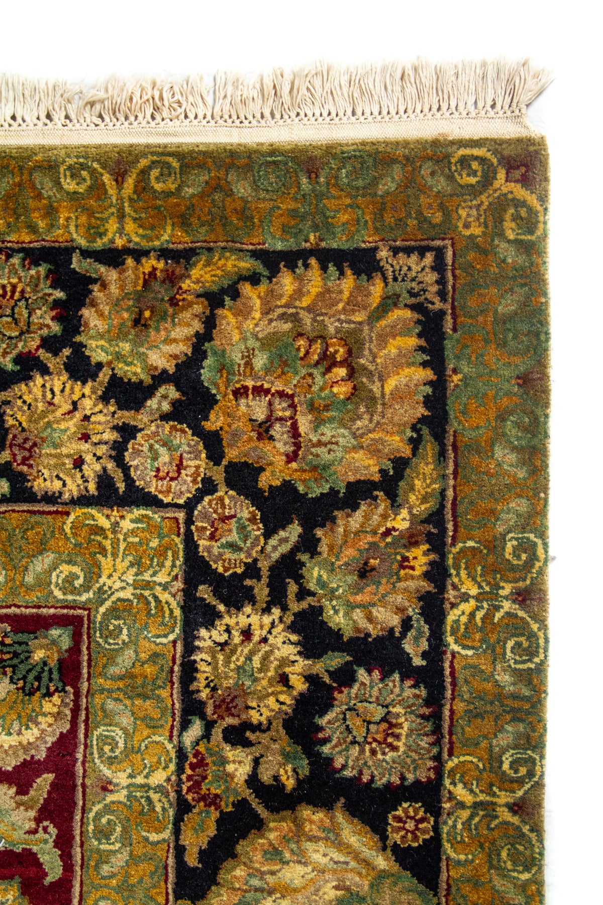 Detalle del borde de alfombra floral con guarda negra, marco verde oliva y flecos claros.