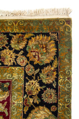 Detalle del borde de alfombra floral con guarda negra, marco verde oliva y flecos claros.