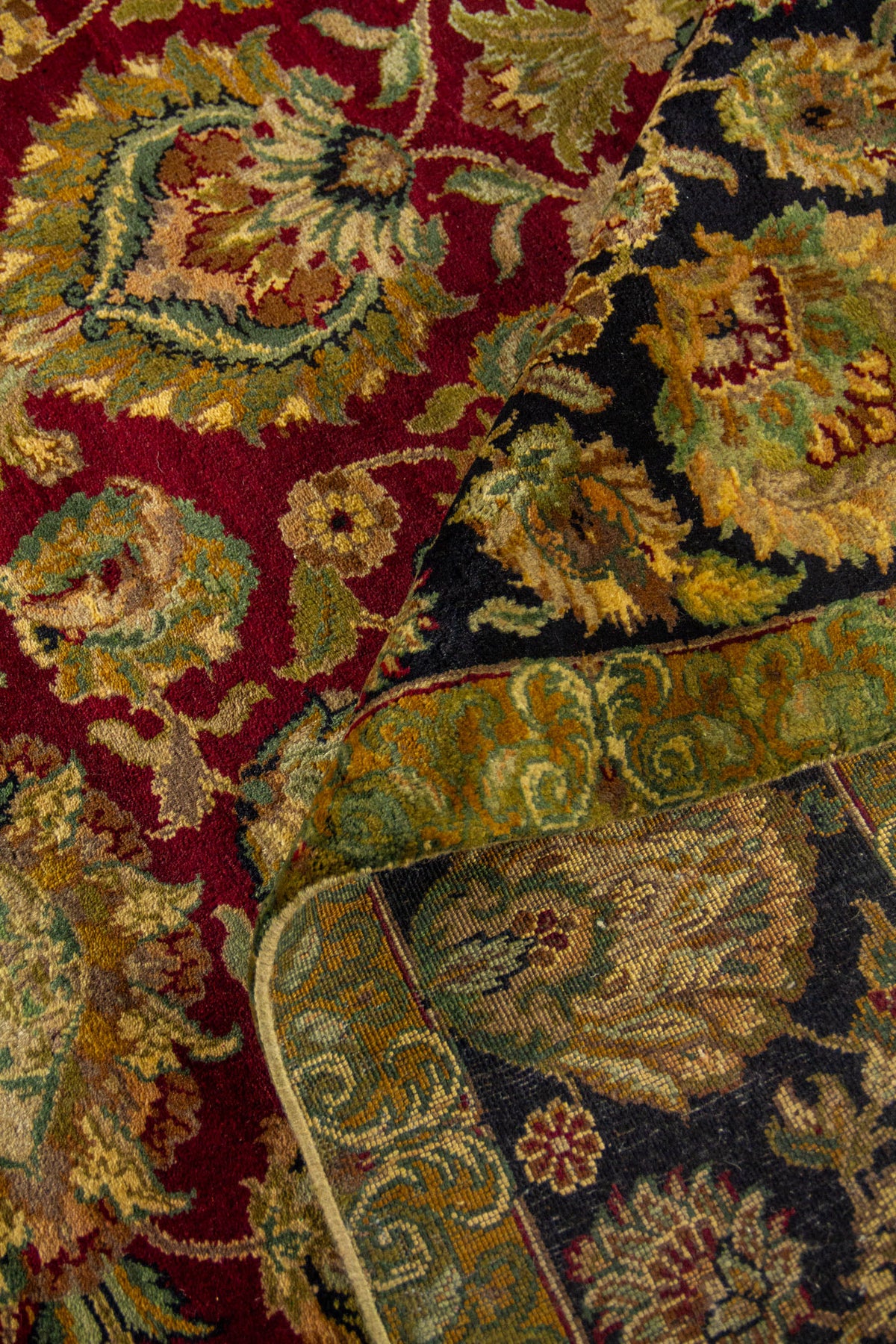 Alfombra doblada mostrando textura, reverso y diseño floral en tonos rojo, negro, beige y verde.