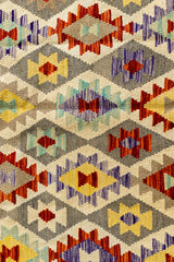 Vista cercana del centro de la alfombra con motivos romboidales en tonos rojo, amarillo, celeste y morado sobre fondo neutro.