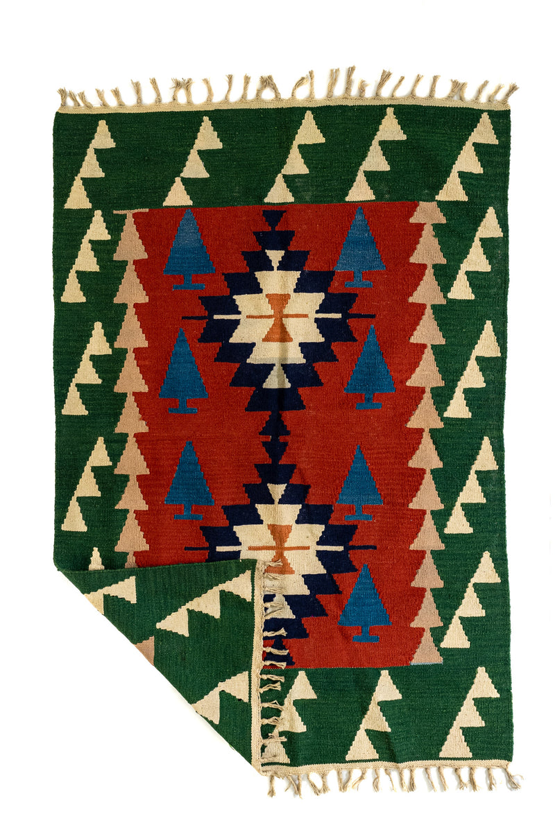 Alfombra kilim doblada en una esquina, mostrando el reverso y los flecos tejidos en tono natural.