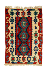 Vista completa de una alfombra kilim con patrón central de rombos escalonados en verde y azul sobre fondo rojo, con guardas geométricas en beige y motivos tribales.