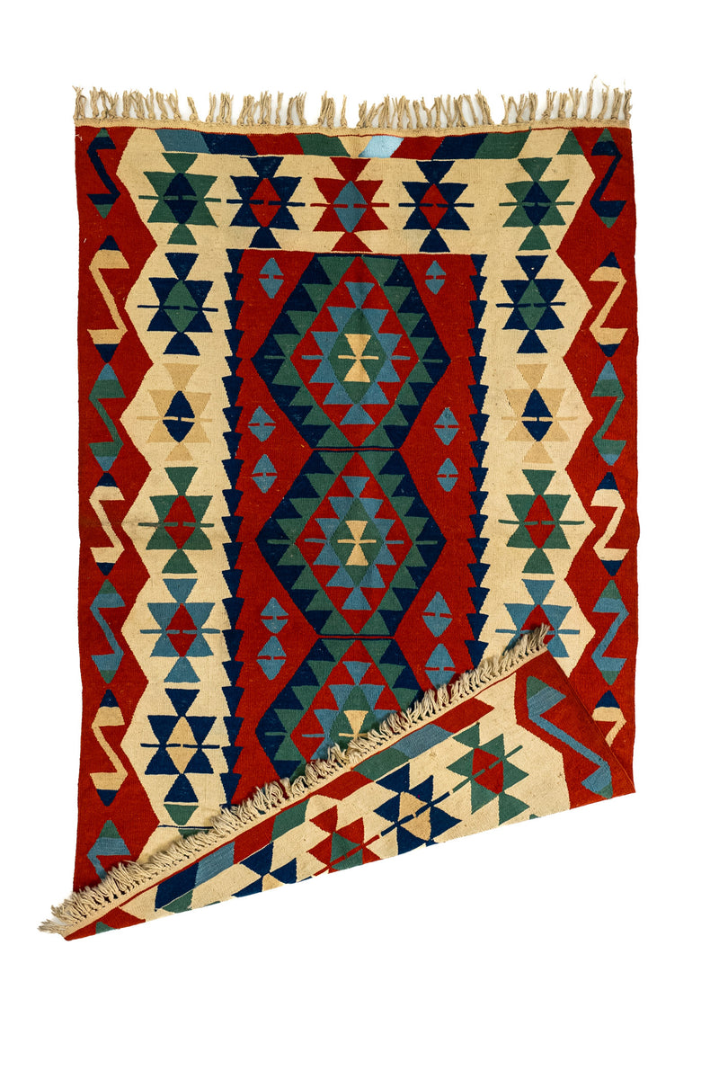 Alfombra kilim con una esquina doblada, mostrando la textura del reverso y los flecos de algodón natural.
