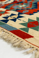 Enfoque bajo y en diagonal del borde inferior de la alfombra kilim, resaltando la textura del tejido y los flecos artesanales.