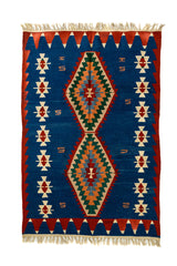 Vista completa de una alfombra kilim con fondo azul intenso, rombos centrales en tonos tierra y guardas rojas con motivos triangulares y símbolos tribales en crema.