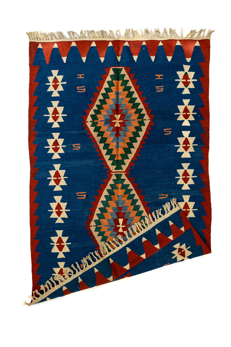 Alfombra kilim con una esquina doblada, mostrando la parte trasera del tejido artesanal y los flecos en color natural.
