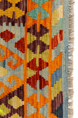 Detalle del borde derecho inferior de la alfombra con motivos escalonados en tonos naranja, azul y vino, enmarcados por flecos cortos.