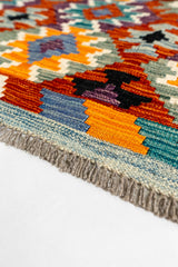 Primer plano del borde inferior, enfocado en la textura del tejido, los flecos y los patrones en azul, naranja y morado.
