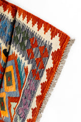 Detalle en ángulo del borde de la alfombra kilim con énfasis en los patrones anaranjado, morado y verde.