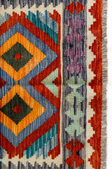 Primer plano del borde derecho de la alfombra kilim, mostrando figuras geométricas entrelazadas en colores vivos.
