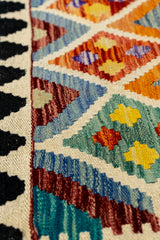Detalle en primer plano del tejido de la alfombra, destacando los colores morado, amarillo, azul y naranja sobre fondo beige.