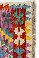 Primer plano del borde superior derecho de la alfombra kilim con detalles en rojo, blanco, turquesa y azul.