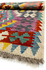 Vista cercana del borde inferior de la alfombra kilim con diseño de cruces geométricas sobre fondo beige y remate de flecos grises.
