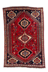 Vista frontal de alfombra estilo Kazak con fondo rojo intenso, medallones geométricos en beige y detalles en azul marino.