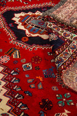 Detalle con esquina levantada de la alfombra, mostrando el reverso, la textura del tejido y el contraste del rojo con el azul marino.