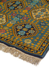 Detalle en perspectiva de alfombra con fondo azul suave, figuras geométricas repetidas y borde decorativo en azul oscuro con acentos dorado.