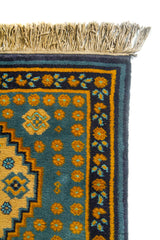 Detalle de esquina de alfombra con guarda azul oscuro, patrones geométricos y fondo azul suave con puntos ornamentales en tono dorado.