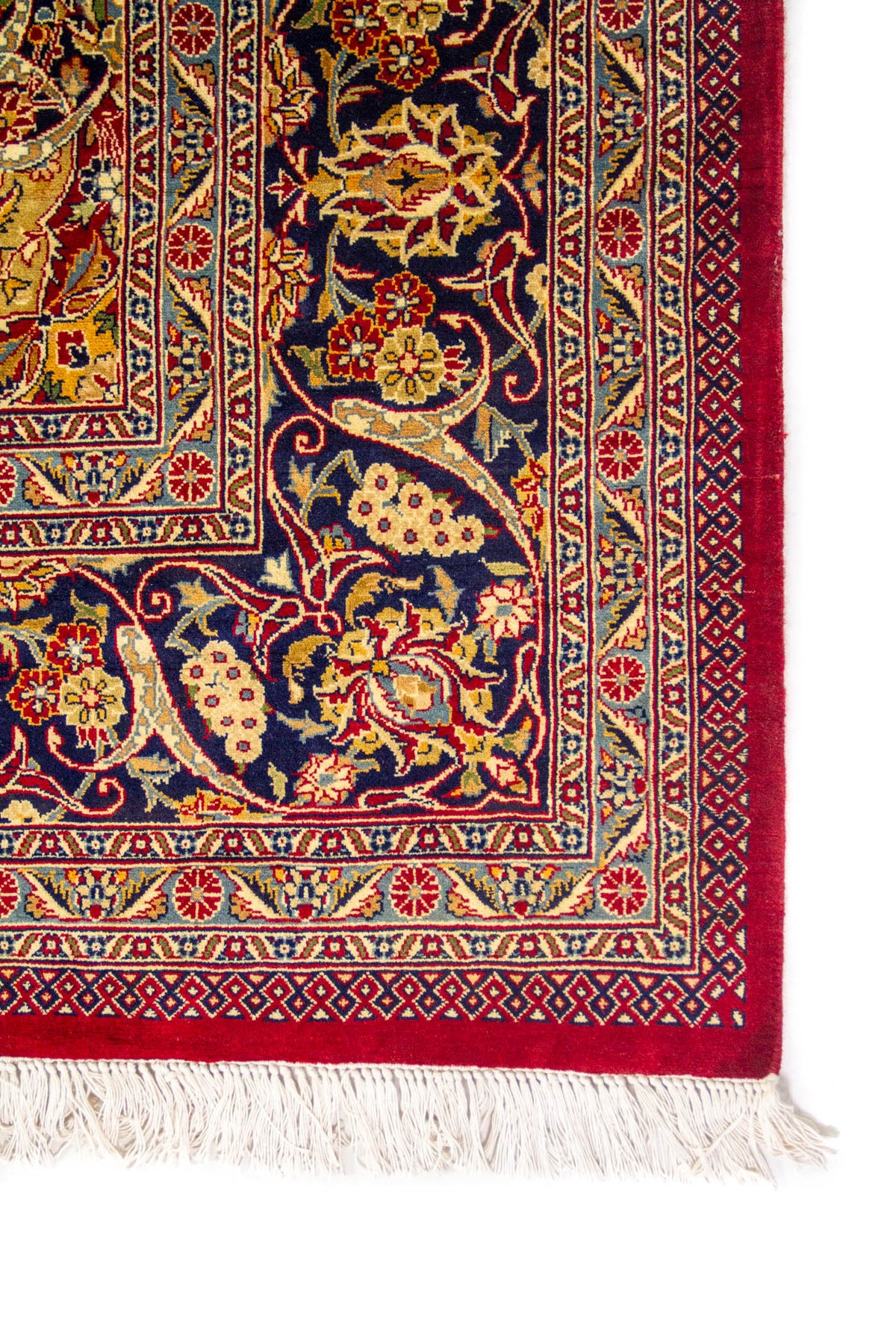Detalle de esquina de alfombra oriental con guarda azul marino, franja roja intensa, motivos florales y flecos claros.
