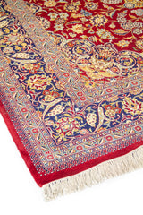 Detalle del diseño floral de alfombra oriental con fondo rojo vibrante, franja azul y líneas ornamentales finamente tejidas.