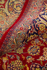Primer plano de alfombra doblada mostrando textura, reverso del tejido y motivos florales en rojo, azul y beige.
