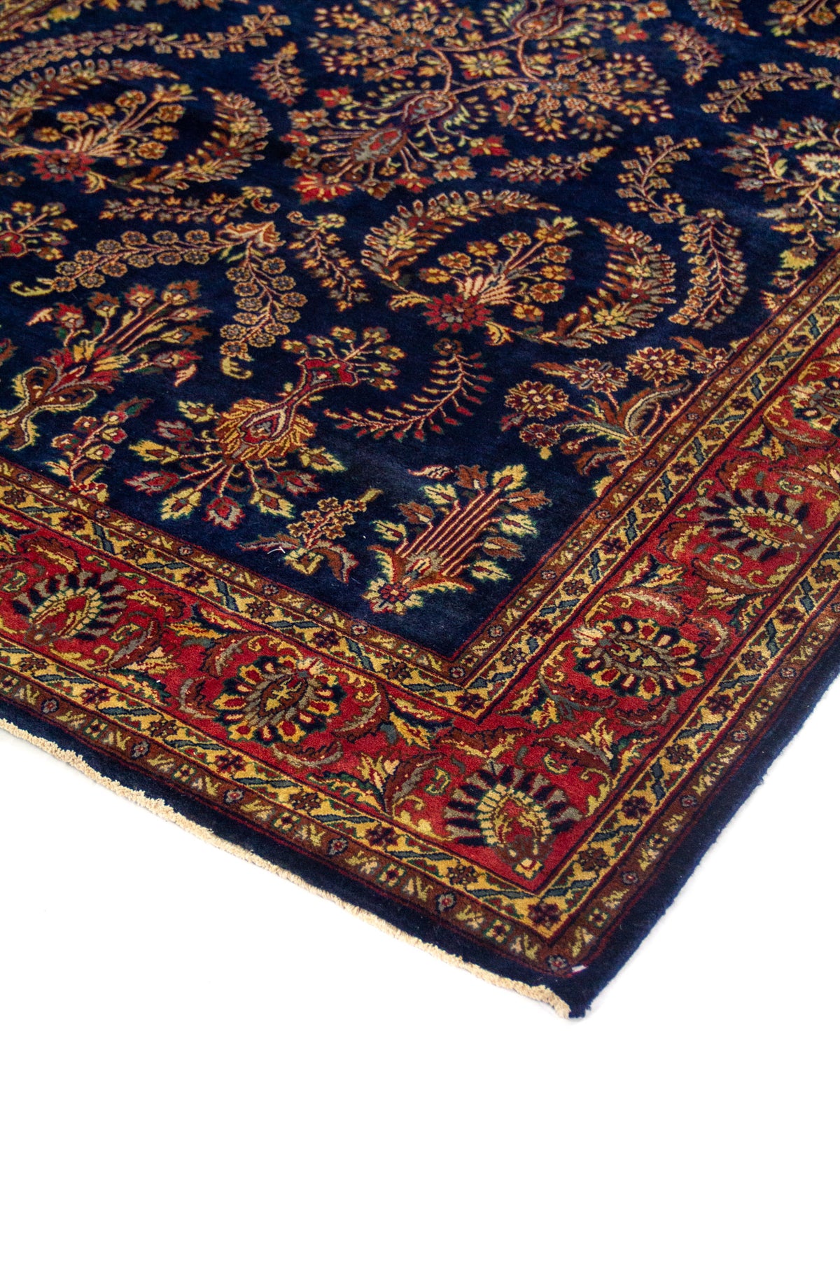 Detalle en perspectiva de alfombra azul marino con borde rojo, diseño floral y terminación con flecos beige.