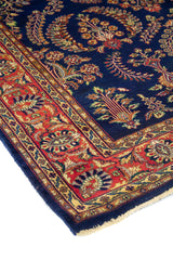 Vista en ángulo de alfombra azul oscura con guarda roja ornamental y delicados motivos botánicos.
