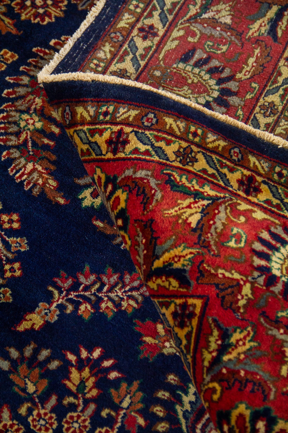 Alfombra azul doblada mostrando su flexibilidad, textura y el contraste entre el campo azul y la guarda roja.