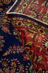 Alfombra azul doblada mostrando su flexibilidad, textura y el contraste entre el campo azul y la guarda roja.